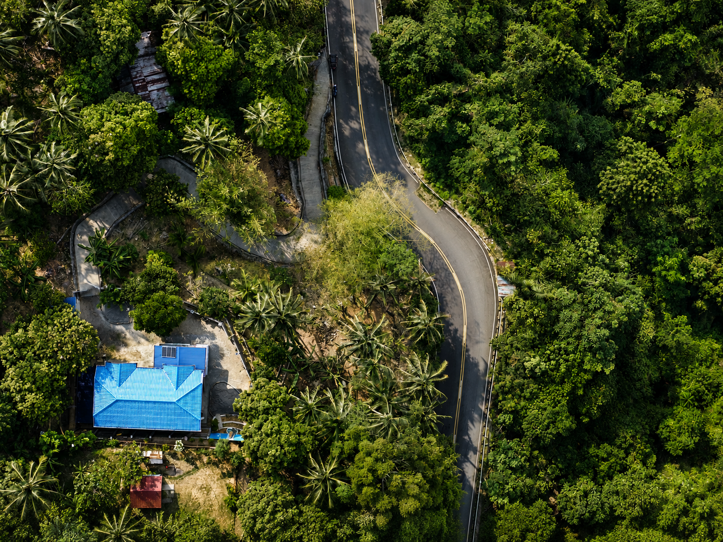 Top-down aerial view of the blue-roofed property and its access from the main road